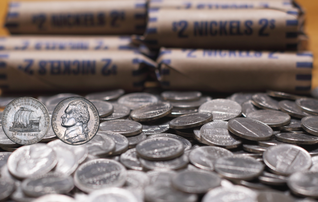 US nickel coins piled in front of two dollar coin rolls.